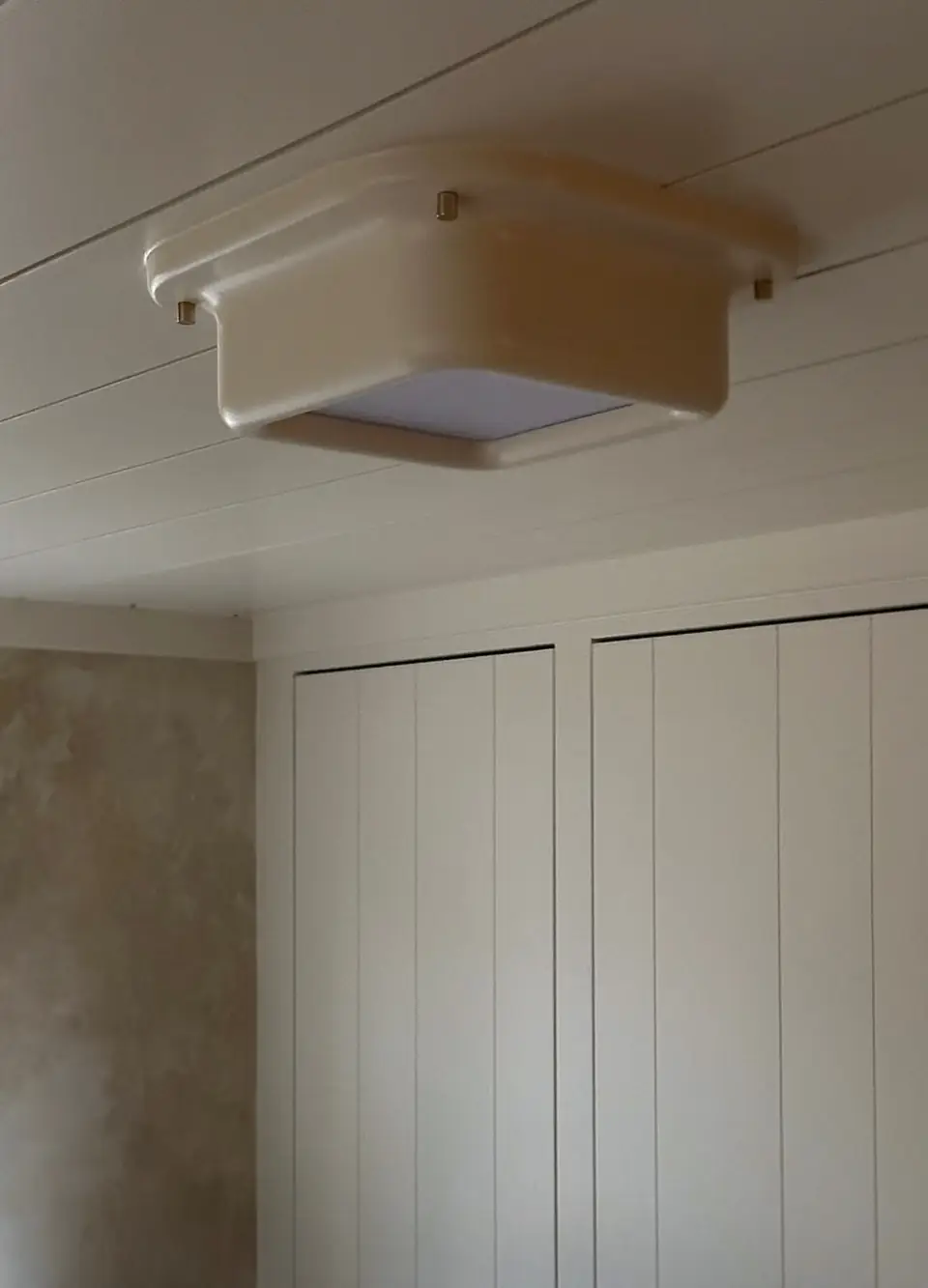 Marshmallow Flush Mount by Brendan Tadler on a white board ceiling, its soft plaster body glowing through a frosted square above a closet of painted panels