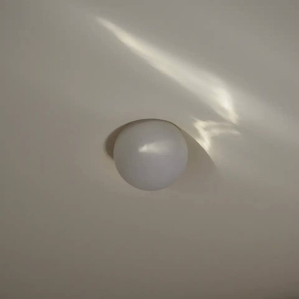 PLST 37 plaster mud-in light by Brendan Tadler, an opal globe rising from a plain plaster ceiling as a streak of sunlight slips past it