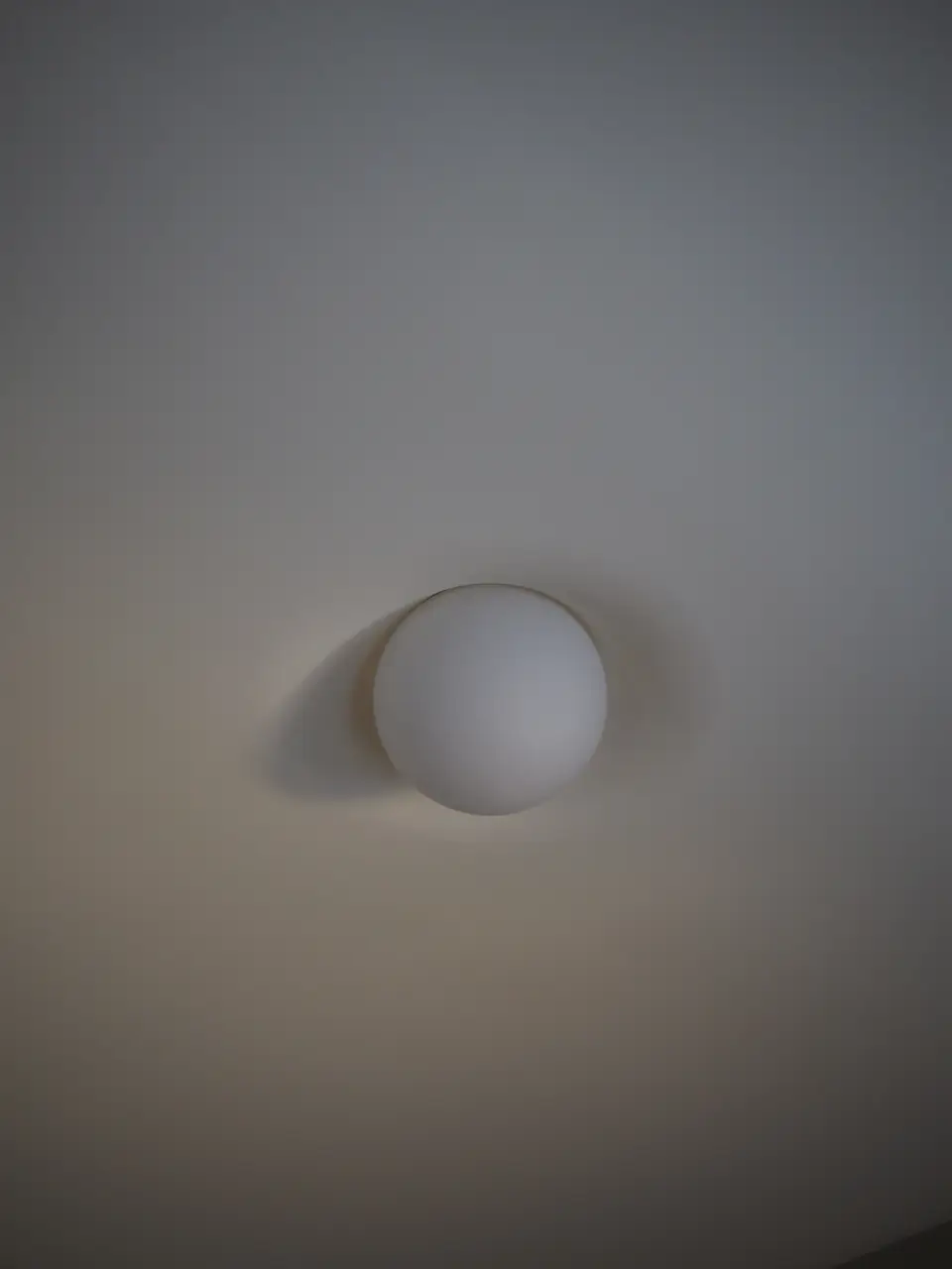 PLST 37 by Brendan Tadler seen from below, the opal globe rising out of a seamless plaster ceiling
