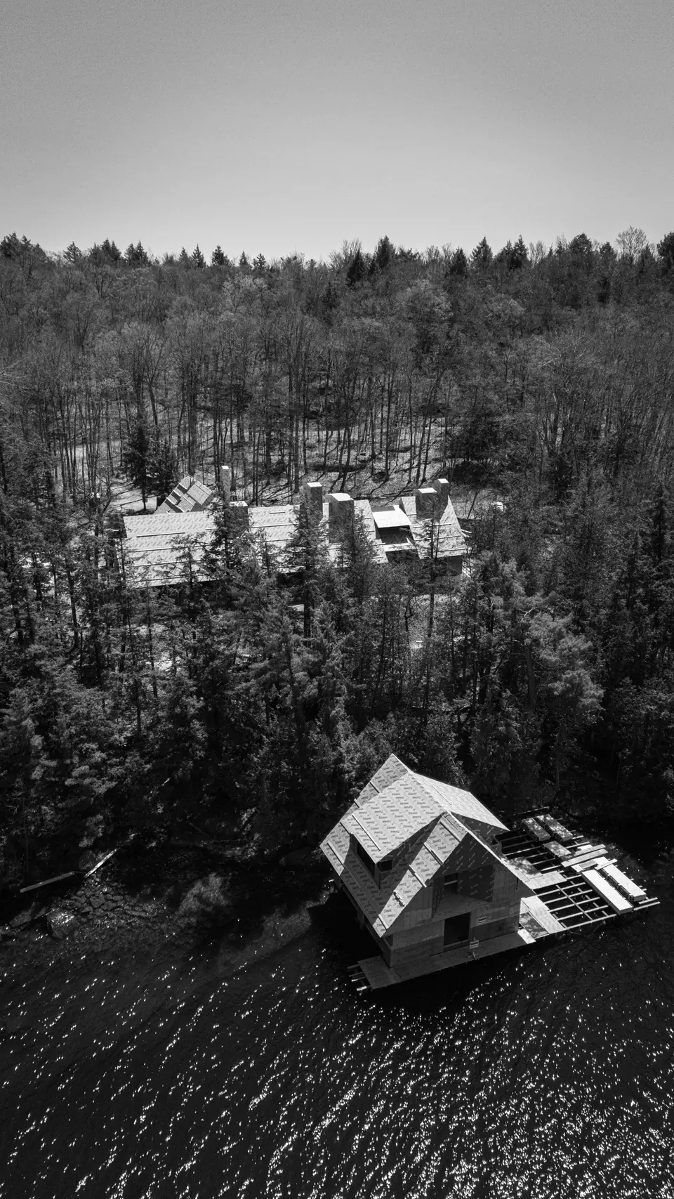 Muskoka Modern Shingle Style house under construction on Lake Muskoka, Ontario: the boathouse on the water in the foreground, with the main house in the trees behind